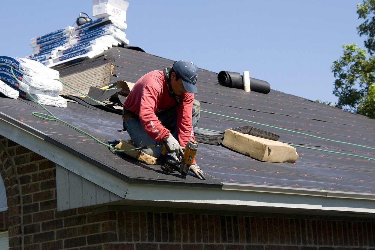 A roofer working on the shingles of a brick home