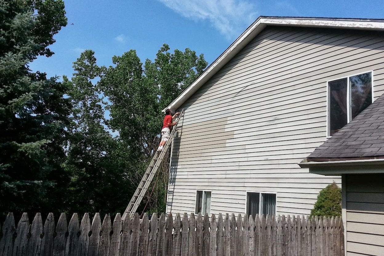 A siding contractor on a ladder repairing vinyl siding on a two-story house