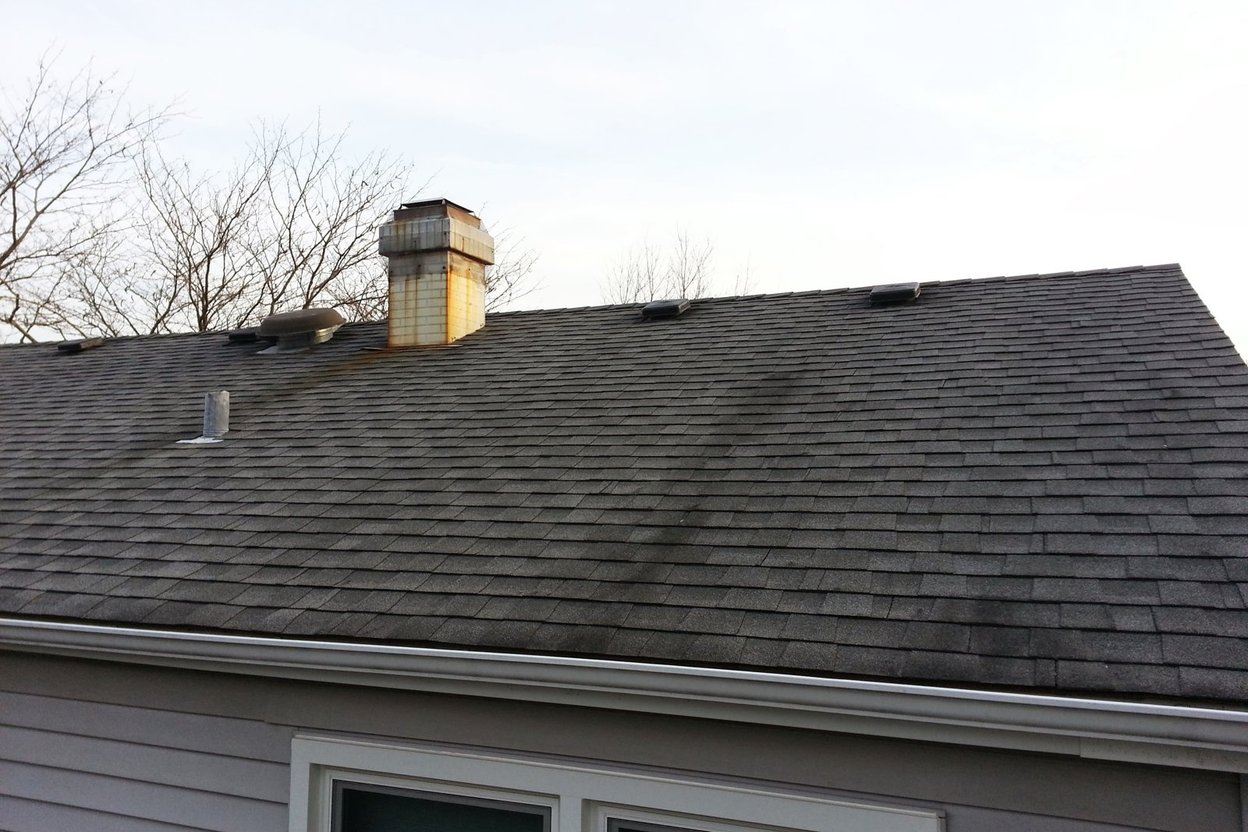 An asphalt shingle roof with dark streaks and a brick chimney, photographed on a job