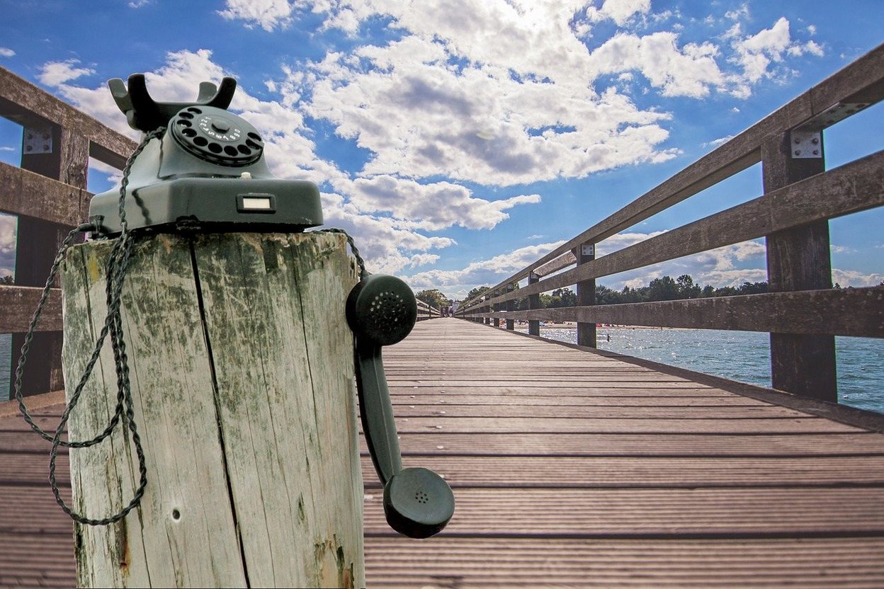 Vintage rotary phone on a wooden pier by the water.