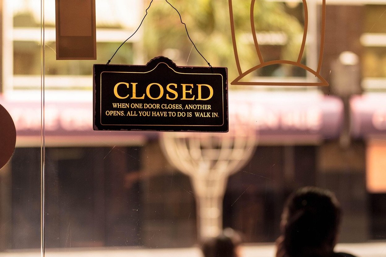 A small-business owner at a shop counter with a closed sign on the door, a holiday wreath nearby, and a phone in hand.