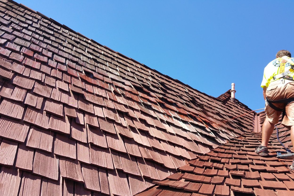 A roofer on a ladder with a phone clipped to his belt, checking a missed call on a sunny job site.