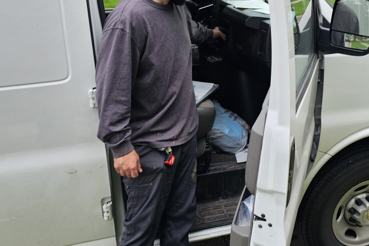 A tradesperson in work clothes checking a missed call on his phone beside a service van at a job site.