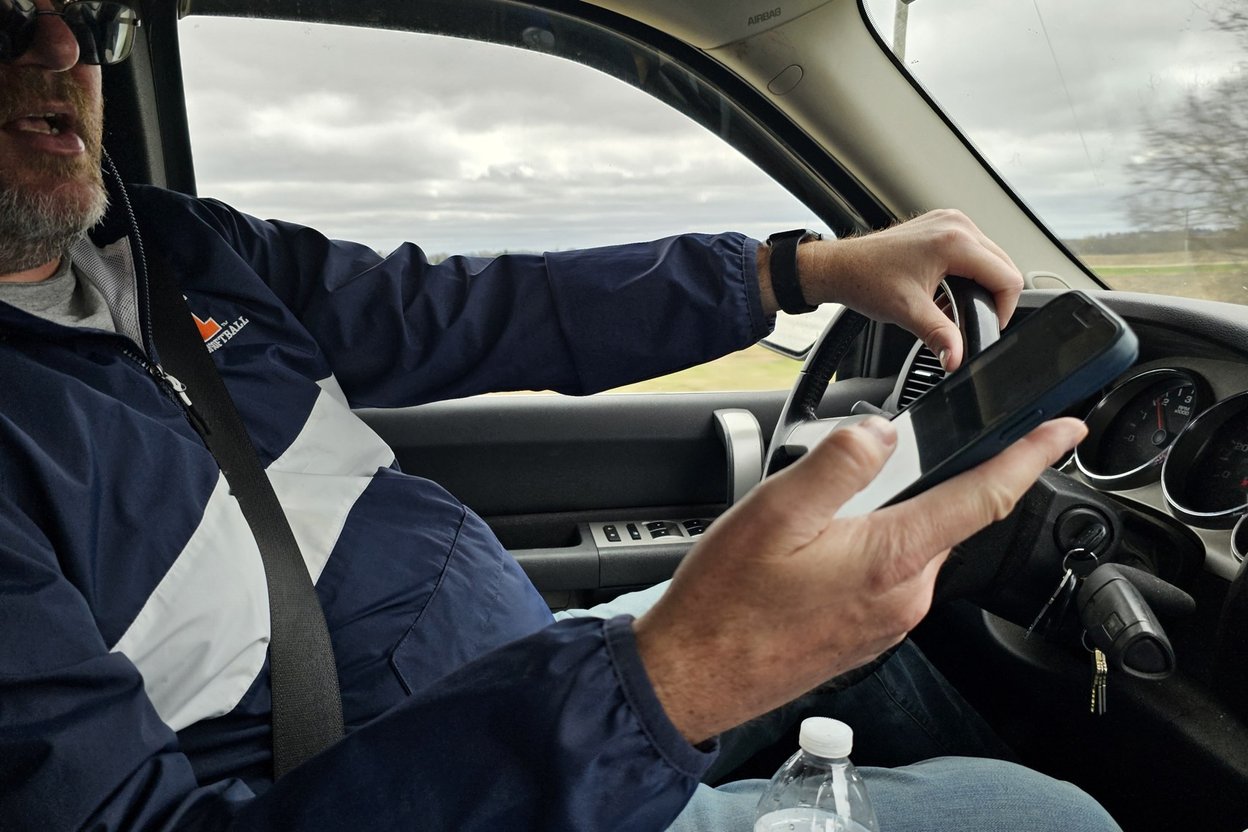 A handyman sitting in an open work truck, phone in hand after a missed call, with tools visible in the toolbox beside him.