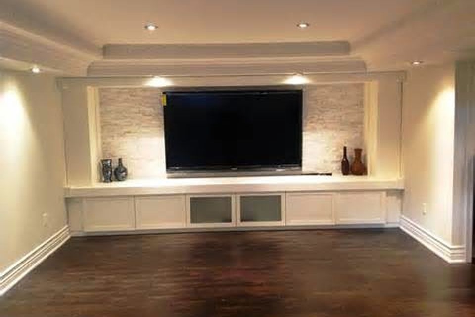 The finished basement: a stone-accent TV wall with built-in cabinets, recessed lighting and dark wood flooring