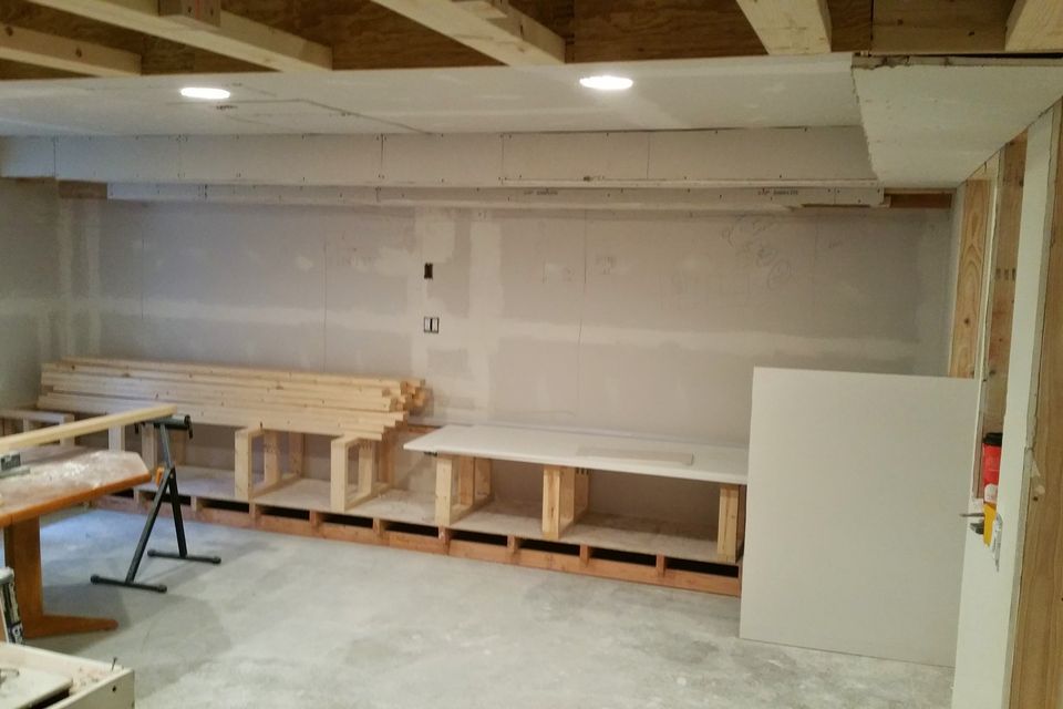 A basement mid-remodel: framed and drywalled walls, recessed lights, and built-in bench bases going in along the wall